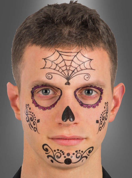 Ein Mann mit kurzen braunen Haaren trägt schwarze und violette „Sugar Skull“-Gesichtsbemalung – mit einem Spinnennetz-Motiv auf der Stirn, verzierten Augenringen, einer schwarzen Nase sowie kunstvollen Details auf den Wangen und am Mund –, die dem „Tattoo Day of the Dead“-Gesichtstattoo ähnelt.