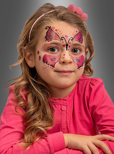 Ein kleines Mädchen mit langen, welligen Haaren und einem rosa Stirnband, das ein rosa Oberteil trägt, hat das „Schmetterling“-Gesichtstattoo für Kinder in Rosa und Schwarz im Gesicht – ideal für Kindergeburtstage oder Karnevalsfeiern.