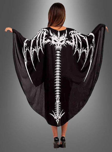 Ein Model trägt den „Drachen-Skelett-Umhang“ mit einem auffälligen Motiv aus einer weißen Fledermaus und einem Wirbelsäulen-Skelett auf dem Rücken; die Arme sind ausgestreckt, um das Design vor einem grauen Hintergrund zur Geltung zu bringen – ideal als Halloween-Kostüm oder Karnevalsumhang.