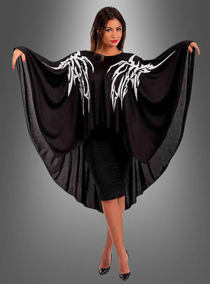 Eine Frau präsentiert das „Drachen Skelett Cape“ – ein schwarzes Kleid mit auffälligen, flügelartigen Fledermausärmeln, die mit markanten weißen Mustern verziert sind – vor einem grauen Hintergrund mit Farbverlauf, was es zu einer auffälligen Wahl als Halloween-Kostüm oder Karnevalsumhang macht.