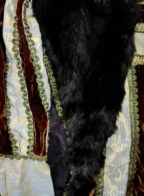Nahaufnahme eines Kleidungsstücks aus braunem Samt, gemustertem blau-weißem Stoff, grüner Borte und einer drapierten schwarzen Pelzstola – ein elegantes Ensemble, das an das „Deluxe Großherzog Herrenkostüm“ erinnert.