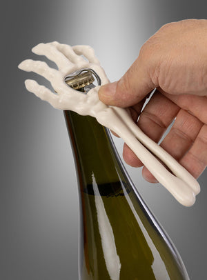 Eine Hand öffnet mit dem Halloween-Flaschenöffner „Skeletthand“, der die Form einer Skelett-Hand hat, eine Weinflasche vor einem grauen Hintergrund – das perfekte Accessoire für Ihre nächste Party.