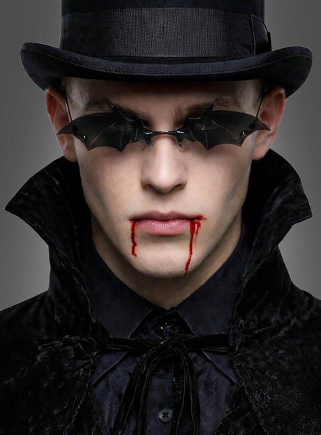 Gekleidet in ein schwarzes, samtenes Gothic-Kostüm und einen Zylinder trägt jemand die auffällige Fledermaus-Brille für Vampire, während rotes Kunstblut aus dem Mund tropft – damit sieht man perfekt wie ein Vampir aus und präsentiert das ultimative Vampir-Accessoire.