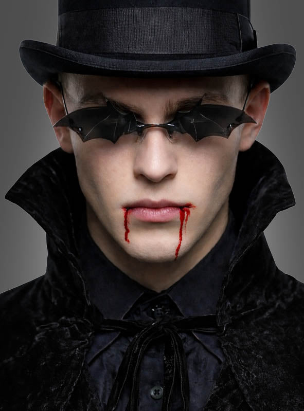 Gekleidet in ein schwarzes, samtenes Gothic-Kostüm und einen Zylinder trägt jemand die auffällige Fledermaus-Brille für Vampire, während rotes Kunstblut aus dem Mund tropft – damit sieht man perfekt wie ein Vampir aus und präsentiert das ultimative Vampir-Accessoire.