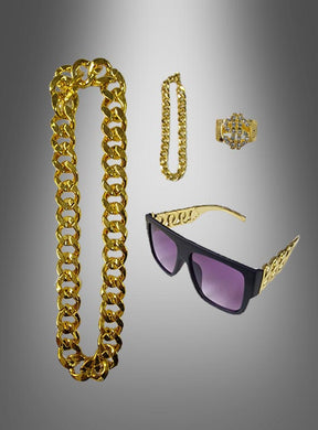 Das 4-teilige „Pimp Dollar“-Schmuckset, bestehend aus einer goldenen Halskette, einem passenden Armband, einem goldenen Ring mit Steinen und einer schwarzen Sonnenbrille mit goldfarbenen Bügeln, wird elegant vor einem grau verlaufenden Hintergrund präsentiert – ideal, jedem Karnevalskostüm einen Hauch von Glamour zu verleihen.