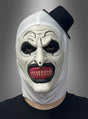Eine Person, die die „Gruselige Clownmaske mit Zylinder“ trägt, mit übertriebener schwarz-weißer Gesichtsbemalung, spitzen Zähnen und einem kleinen, schräg sitzenden Zylinderhut, vor einem grauen Hintergrund.
