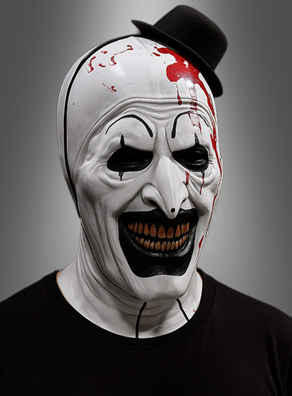Eine Person, die die „Blutige Clown-Maske schwarz-weiß“ trägt, mit schwarzen Akzenten, übertriebenen Zähnen, Blutspritzern und einem kleinen schwarzen Hut, vor einem neutralen Hintergrund mit Farbverlauf.