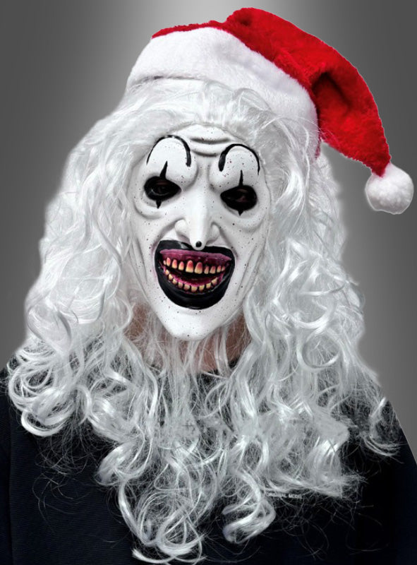 Eine Person, die die „Horrorclown-Maske mit Weihnachtsmütze“ trägt, mit gruseligen weißen Details, schwarzen Akzenten, langen weißen Haaren und einer roten Weihnachtsmütze, die an „Art the Clown“ erinnert, vor einem grauen Hintergrund.
