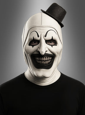 Eine Person, die eine schwarz-weiße Clownmaske mit Zylinder trägt, mit übertriebenem schwarzem Make-up, einem breiten Grinsen und einem kleinen, schräg sitzenden schwarzen Hut, vor einem grauen Hintergrund.