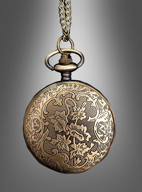 Eine antike Taschenuhr in Goldoptik mit funktionierendem Uhrwerk und aufwendigen Blumengravuren hängt an einer Kette vor einem grauen Hintergrund mit Farbverlauf.