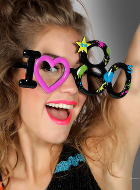 Eine Frau mit der „I love 80s Partybrille Unisex“, die einen knalligen Lippenstift, einen offenen Mund und einen erhobenen Arm vor grauem Hintergrund zeigt – perfekt als witziges Kostümzubehör für jede Retro-Party.