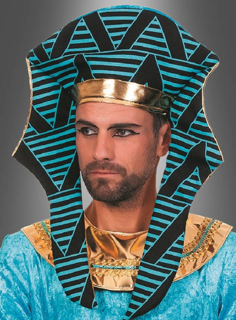 Ein Mann, der einen gestreiften, türkis-schwarzen Pharao-Kopfschmuck und einen goldenen Kragen trägt und ein auffälliges blaues Pharao-Kostüm mit dunklem Eyeliner trägt, posiert vor einem grauen Hintergrund.