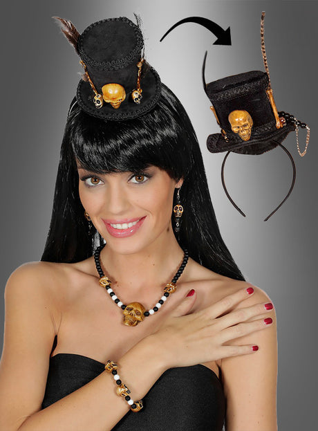Eine Frau trägt das Voodoo-Schmuckset mit Minizylinder – bestehend aus einem schwarzen, trägerlosen Oberteil, einer schwarzen Perücke, einer Halskette mit Totenkopf-Motiv, einem Armband, Ohrringen und einem kleinen schwarzen Hut, der mit einem goldenen Totenkopf verziert ist – perfekte Halloween-Accessoires für jedes Voodoo-Zauberin-Kostüm; Eine Einblendung zeigt das detaillierte Design des Minizylinders.