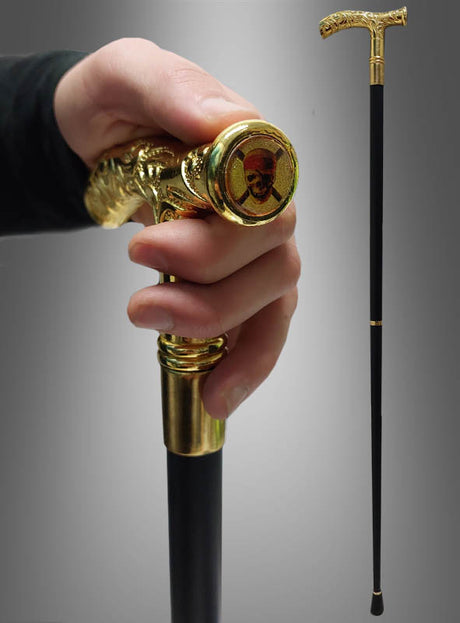 Eine Hand, die den „Edler Gehstock mit goldenem Griff 93 cm“ hält – einen stilvollen schwarzen Gehstock mit einem kunstvoll verzierten goldenen Totenkopfgriff, der sich ideal als Kostümzubehör für dramatische Outfits eignet; der komplette „Edler Gehstock mit goldenem Griff 93 cm“ ist rechts abgebildet.