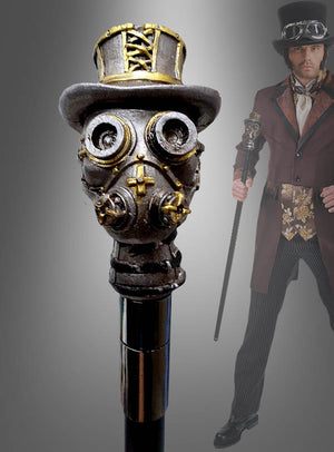 Im Hintergrund hält eine Person in einem Steampunk-Kostüm den „Deluxe Gehstock Steampunk“ – einen im Steampunk-Stil gestalteten Spazierstock mit einem Griff in Form einer Gasmaske, die einen Zylinder trägt – als auffälliges Kostümzubehör in der Hand.