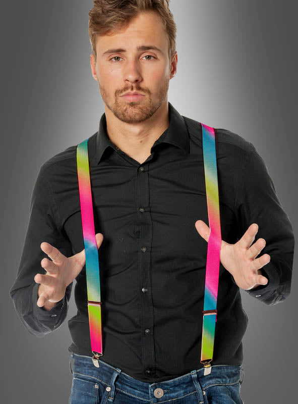Ein Mann in schwarzem Hemd und Jeans trägt Hosenträger in Neon-Regenbogenfarben und gestikuliert mit beiden Händen vor einem grauen Hintergrund mit Farbverlauf, was dem Ganzen eine verspielte Note verleiht, die an ein Accessoire eines Clownkostüms erinnert.