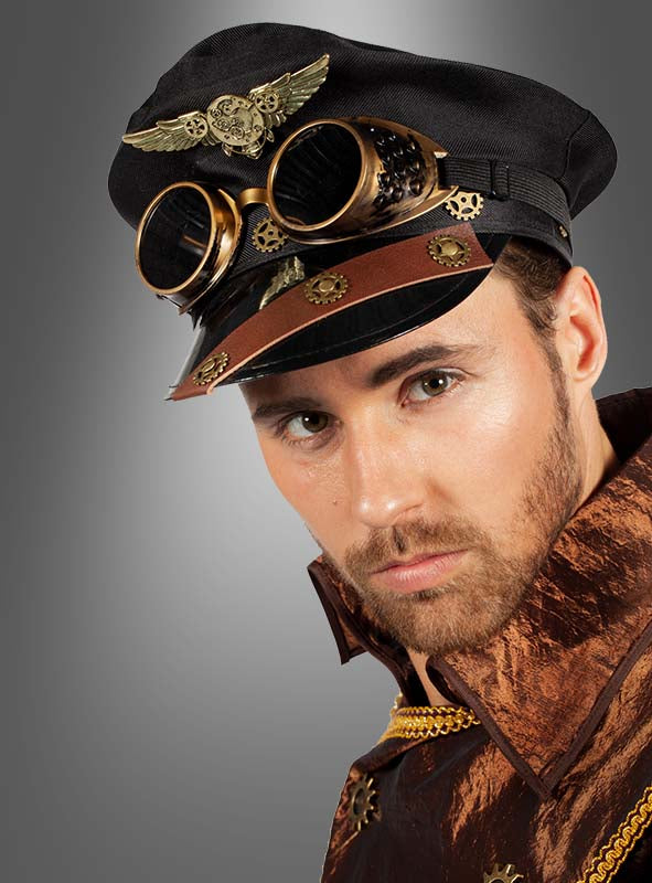 Ein Mann trägt einen schwarzen Steampunk-Hut mit Schutzbrille (Steampunk-Mütze mit Brille, schwarz), Messingzahnrädern und einem braunen, metallisch anmutenden Outfit vor einem schlichten grauen Hintergrund.