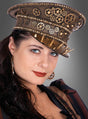 Vor einem grauen Hintergrund steht eine Frau, die eine braune Steampunk-Schildmütze Deluxe Unisex trägt, die mit Zahnrädern und Stacheln verziert ist, sowie langes dunkles Haar, Creolen und ein gestreiftes braunes Steampunk-Kostüm.