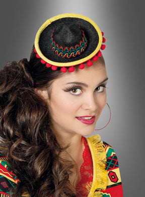 Hier ist Ihr umformulierter Satz unter Verwendung der bereitgestellten Produktdaten: Eine Frau mit langen braunen Haaren trägt den „Mini Sombrero Hut für Mexikanerin“ – mit gelber Borte und roten Bommeln, befestigt an einem Haarreif – zusammen mit einem farbenfrohen, gemusterten Oberteil, wodurch vor einem grauen Hintergrund ein festliches Kostüm entsteht.