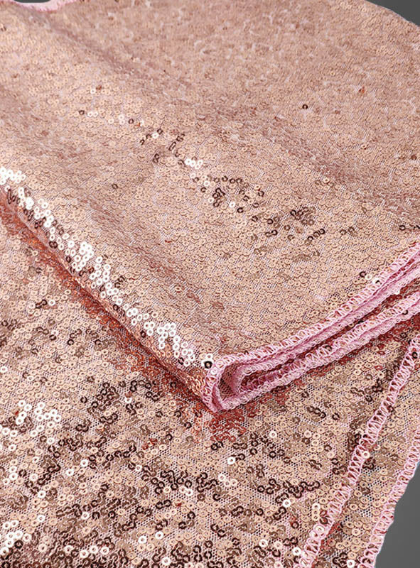 Auf grauem Hintergrund ist gefalteter Stoff in Roségold zu sehen, der mit glänzenden Pailletten übersät ist – perfekt in Kombination mit dem „Funkelndes Party-Dekoset Roségold 35 Teile“ für eine unvergessliche Feier.