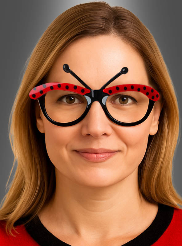 Eine Frau trägt die „Brille für Marienkäfer rot-schwarz“, ein ausgefallenes Accessoire in Form eines Marienkäfers mit rotem Rahmen und schwarzen Punkten vor grauem Hintergrund – ein auffälliges Käfer-Kostüm-Accessoire, das sich ideal für jeden Anlass eignet.