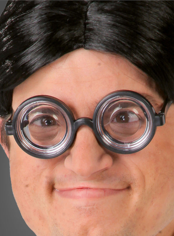 Nahaufnahme einer Person, die die „Hornbrille Karneval für Nerds“ trägt – eine dicke, runde schwarze Brille im beliebten Nerd-Stil der Spaßbrillen – sowie eine schwarze Perücke; sie lächelt leicht vor einem neutralen grauen Hintergrund.