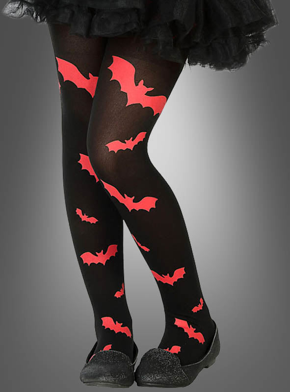 Ein Kind präsentiert die „Strumpfhose mit Fledermäusen für Kinder“ – eine schwarze Strumpfhose mit leuchtend roten Fledermausmotiven –, kombiniert mit einem schwarzen Rock und passenden schwarzen Schuhen, vor einem grauen Hintergrund mit Farbverlauf. Ideal als Fledermaus-Accessoire oder als Teil eines Halloween-Kostüms für Kinder.