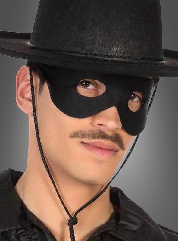 Eine Person mit einem schwarzen Hut mit breiter Krempe, einer „Schwarzen Ganoven-Augenmaske“ und schwarzer Kleidung, die einen dünnen Schnurrbart trägt und in die Kamera blickt – perfekt für ein Karnevalskostüm.