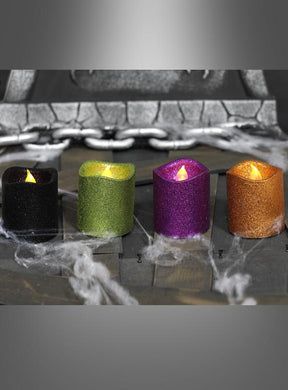 Vier glitzernde LED-Kerzen (8 cm) als Halloween-Tischdekoration in Schwarz, Grün, Lila und Orange sind nebeneinander auf einer Holzunterlage angeordnet; im Hintergrund sorgen künstliche Spinnweben und eine Kette für die perfekte Stimmung – ideal als Partydekoration für jeden festlichen Anlass.