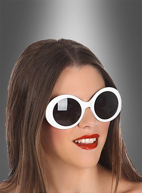 Eine Frau mit glattem braunem Haar trägt die Brille „Jackie 60er Jahre“ in Weiß und roten Lippenstift und lächelt vor einem grauen Hintergrund mit Farbverlauf.