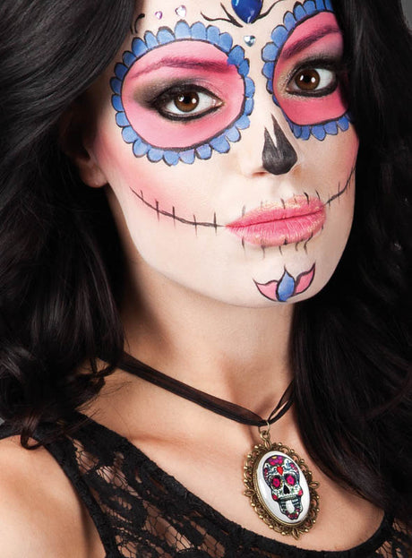 Eine Frau mit schwarzen Haaren trägt Gesichtsbemalung im Stil des „Tages der Toten“ (Zuckerschädel), rosa Lidschatten und die „Sugar Skull“-Halskette – eine elegante Halskette mit einem Totenkopf-Anhänger, der von traditionellem mexikanischem Totenkopfschmuck inspiriert ist.