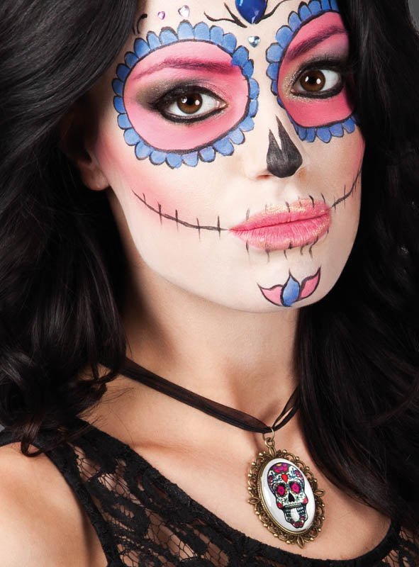 Eine Frau mit schwarzen Haaren trägt Gesichtsbemalung im Stil des „Tages der Toten“ (Zuckerschädel), rosa Lidschatten und die „Sugar Skull“-Halskette – eine elegante Halskette mit einem Totenkopf-Anhänger, der von traditionellem mexikanischem Totenkopfschmuck inspiriert ist.