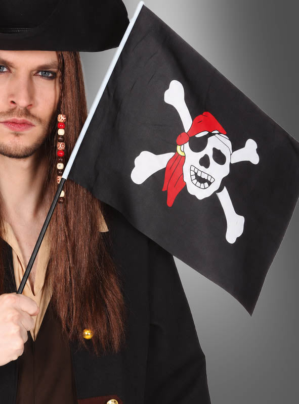 Eine Person in einem Piratenkostüm hält die „Totenkopf Piratenflagge“ (43 cm) mit einem Totenkopf-Motiv (Jolly Roger) in der Hand und trägt ein rotes Bandana – perfekt für jede Piratenparty.