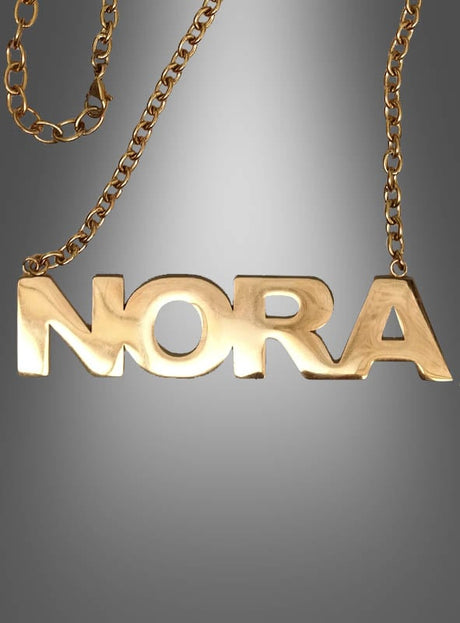 Deluxe-NORA-Kette für Pop-Duo: Eine goldene Metallkette mit einem Anhänger, auf dem „NORA“ in auffälligen Großbuchstaben zu sehen ist – die ideale Wahl für eine stilvolle 80er-Jahre-Mottoparty. Präsentiert wird sie vor einem eleganten grauen Farbverlauf.