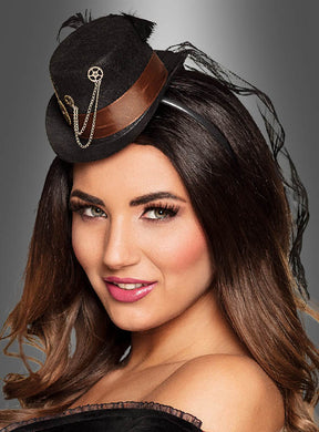 Eine Frau trägt den „Zahnrad Minizylinder Steampunk“ – einen schwarzen Miniaturhut mit braunem Band, goldener Kette und Zahnradverzierungen – ein elegantes Damenaccessoire, das sich ideal für jedes Steampunk-Kostüm eignet, vor einem grauen Hintergrund mit Farbverlauf.