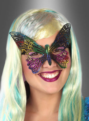 Eine lächelnde Person mit langen, hellblauen und blonden Haaren trägt eine bunte Augenmaske „Schmetterling bunt“ im Gesicht – das perfekte Accessoire für einen Maskenball – vor einem grauen Hintergrund mit Farbverlauf.