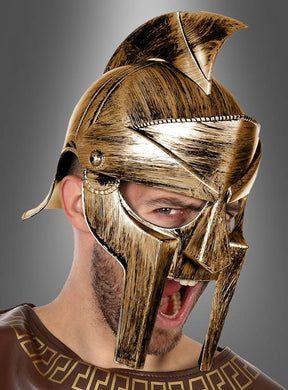 Vor einem grauen Hintergrund steht eine Person, die den goldfarbenen „Antiker Römerhelm“ trägt – einen gold- und bronzefarbenen Helm im antiken griechischen oder römischen Stil mit offenem Mund, der möglicherweise gerade schreit.