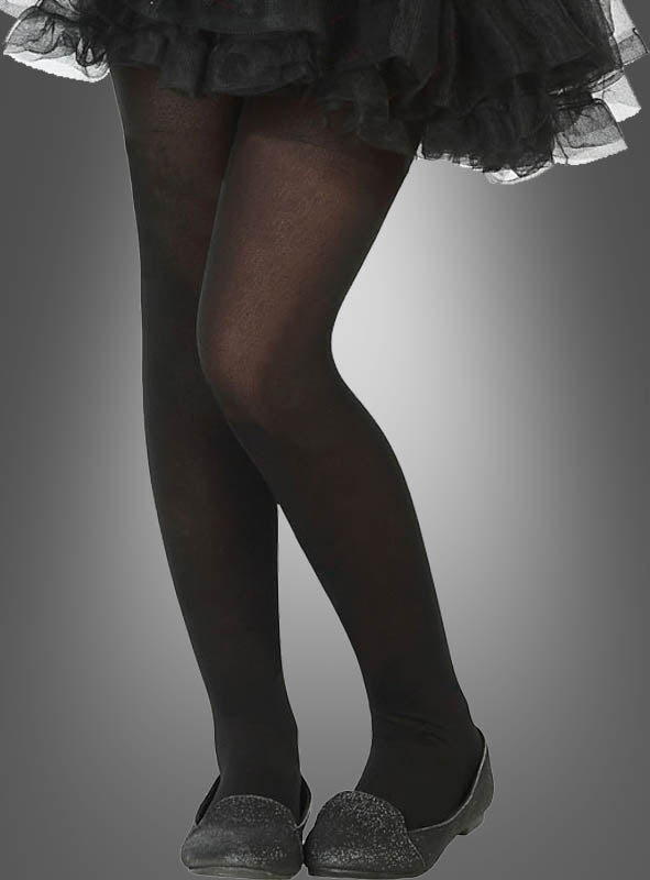 Eine Person trägt die Nylon-Strumpfhose „Kinder schwarz“, dazu einen schwarzen Rüschenrock und schwarze flache Schuhe, und steht mit überkreuzten Beinen vor einem grauen Hintergrund mit Farbverlauf.