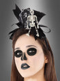 Eine Person mit dunklem, schädelartigem Make-up trägt einen „Skelett Haarreif Halloween“, der mit einem kleinen Skelett und einem Grabstein verziert ist, vor einem grauen Hintergrund mit Farbverlauf.