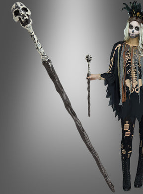 Eine Person in einem Skelettkostüm, die das „Voodoo Zepter 44 cm mit Totenkopf“ vor einem grau abgestuften Hintergrund hält – ein auffälliges Halloween-Accessoire, ideal für jeden gruseligen Anlass.