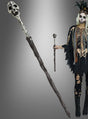 Eine Person in einem Skelettkostüm, die das „Voodoo Zepter 44 cm mit Totenkopf“ vor einem grau abgestuften Hintergrund hält – ein auffälliges Halloween-Accessoire, ideal für jeden gruseligen Anlass.