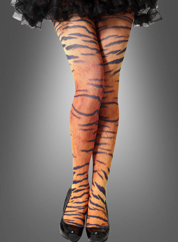 Ein Model präsentiert die Strumpfhose mit Tigermuster und kombiniert die Strumpfhose mit Tigermuster mit schwarzen High Heels, während sie mit gekreuzten Beinen vor einem schlichten grauen Hintergrund steht.