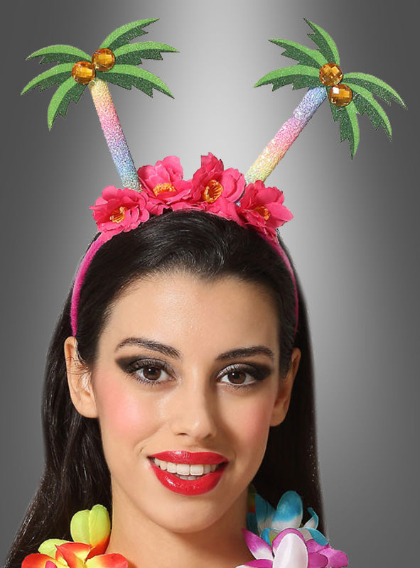 Eine Frau, die einen Haarreif „Südseetraum mit Blumen“ mit glitzernden Palmen und rosa Blumen trägt, kombiniert mit einer bunten Blumen-Lei – ein perfektes Accessoire für eine Hawaii-Party – vor einem grauen Hintergrund mit Farbverlauf.