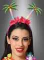 Eine Frau, die einen Haarreif „Südseetraum mit Blumen“ mit glitzernden Palmen und rosa Blumen trägt, kombiniert mit einer bunten Blumen-Lei – ein perfektes Accessoire für eine Hawaii-Party – vor einem grauen Hintergrund mit Farbverlauf.