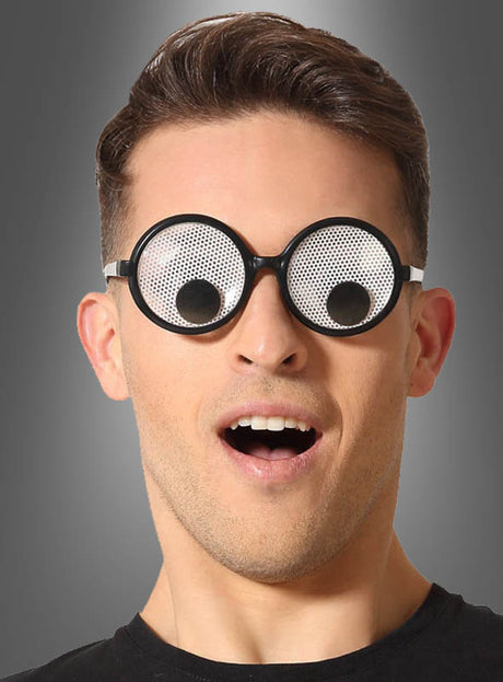 Ein Mann, der eine runde „Partybrille mit Wackelaugen“ trägt – eine lustige Brille mit großen, cartoonartigen, wackelnden Augen auf den Gläsern und einem vor Überraschung geöffneten Mund vor einem grauen Farbverlaufshintergrund – ein witziges Kostüm-Accessoire, das sich perfekt für jeden verspielten Anlass eignet.