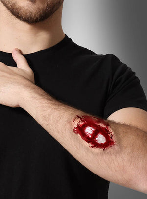 Eine Person in einem schwarzen T-Shirt präsentiert die „Wunde offener Knochenbruch“ – eine realistisch wirkende künstliche Wunde mit freiliegendem Knochen am Unterarm, die sich perfekt für ein Zombie-Kostüm oder zur Erzeugung eines eindrucksvollen Make-up-Effekts eignet.