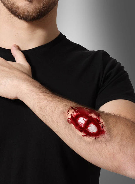 Eine Person in einem schwarzen T-Shirt präsentiert die „Wunde offener Knochenbruch“ – eine realistisch wirkende künstliche Wunde mit freiliegendem Knochen am Unterarm, die sich perfekt für ein Zombie-Kostüm oder zur Erzeugung eines eindrucksvollen Make-up-Effekts eignet.