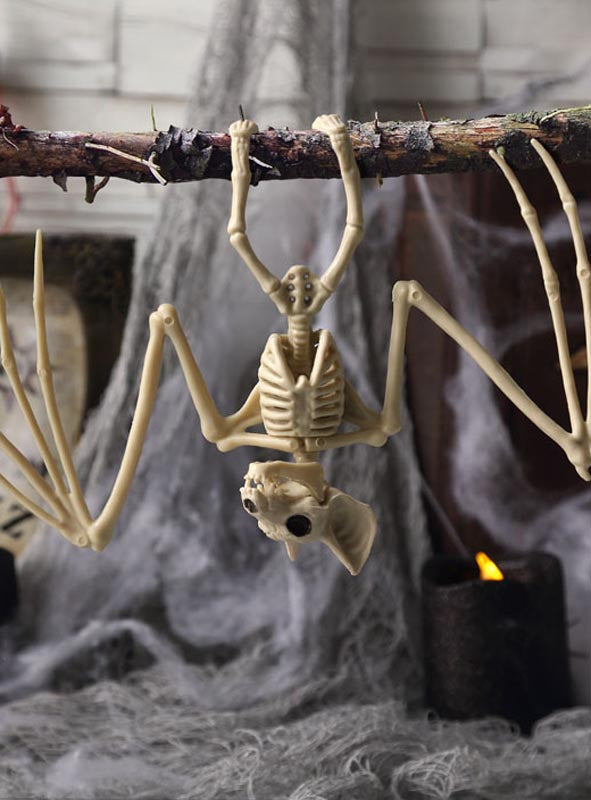 Die Dekoration „Skelett-Fledermaus“ (17 x 30 cm) hängt kopfüber an einem Ast, umgeben von Spinnweben und einer leuchtenden schwarzen Kerze im Hintergrund – perfekt, um Ihrer Halloween-Dekoration einen gruseligen Touch zu verleihen.