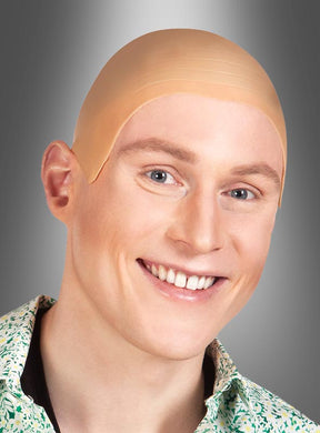 Eine lächelnde Person, die eine beige Latex-Glatzkopf-Perücke trägt – perfekt für den Karneval –, vor einem grauen Hintergrund mit Farbverlauf.