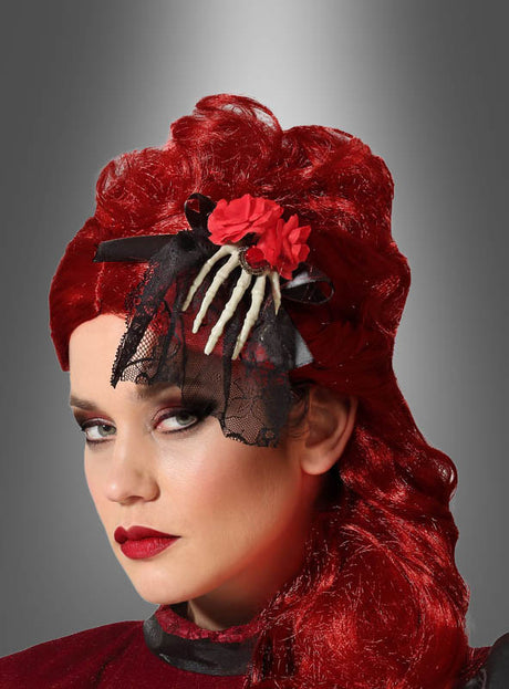 Eine Person mit leuchtend roten Haaren und auffälligem Make-up trägt die Halloween-Haarspange „Tag der Toten“ – eine schwarze Haarspange aus Spitze, verziert mit roten Blumen und einer Skeletthand, inspiriert vom Día de los Muertos – vor einem grauen Hintergrund mit Farbverlauf.